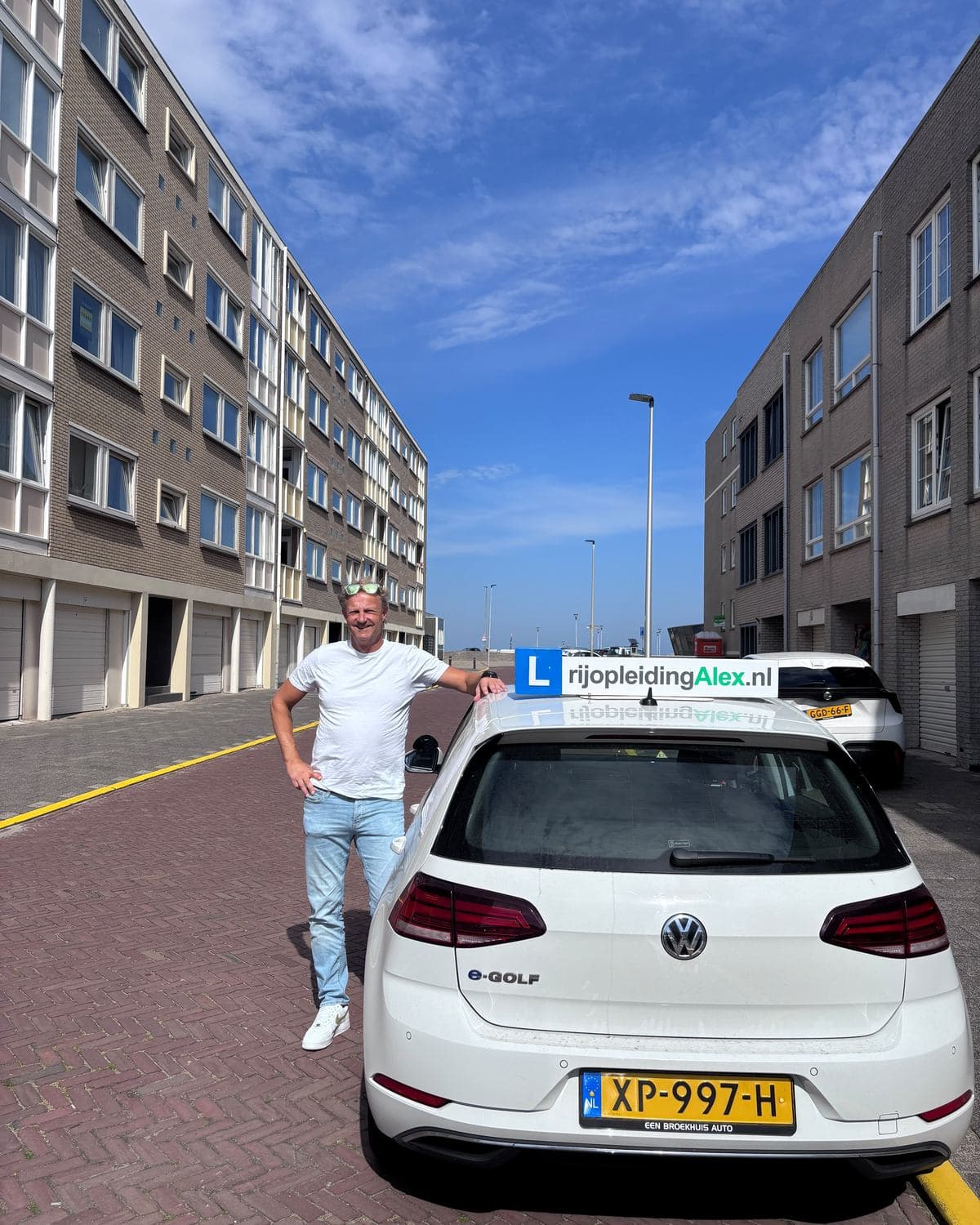 Alex van Rijopleiding Alex bij de lesauto, een witte Volkswagen e-Golf, aan de kust in IJmuiden.